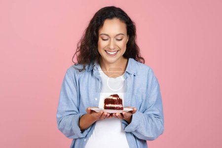 Foto de Feliz joven embarazada atractiva con ropa casual sosteniendo delicioso pastel, disfrutando del postre, anhelo de dulces, aislado en el fondo del estudio rosa. Alimentos poco saludables durante el embarazo - Imagen libre de derechos