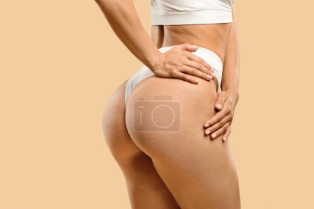 Photo for Unrecognizable young fit woman in white underwear showing smooth silky skin on her buttocks, cropped shot of athletic female in lingerie posing over beige studio background, copy space - Royalty Free Image
