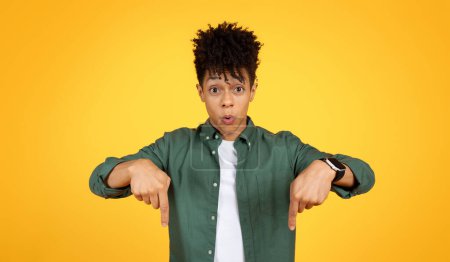 Photo for Amazed stylish handsome young black guy pointing down at copy space for advertisement, showing nice offer, deal, isolated on yellow studio background, banner - Royalty Free Image