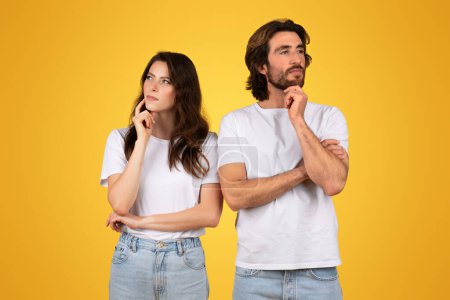 Téléchargez les photos : Couple européen pensif en t-shirts blancs et jeans bleus, debout dos à dos avec des expressions réfléchies, regardant vers le haut et loin dans la contemplation sur un fond jaune - en image libre de droit