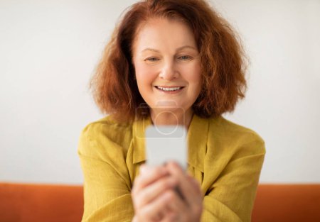 Téléchargez les photos : Gros plan d'une femme âgée souriante utilisant son smartphone à la maison, message de dame âgée heureuse sur son téléphone mobile, magasinage en ligne ou navigation sur Internet, profiter des technologies modernes, espace libre - en image libre de droit