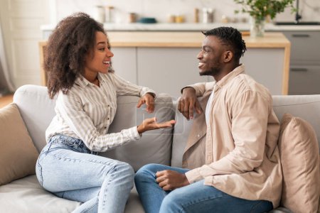 Photo for Cheerful Black Young Spouses Talking Enjoying Their Conversation And Flirt During Domestic Romantic Weekend, Sitting Together On Couch And Chatting At Modern Home Interior In Living Room - Royalty Free Image