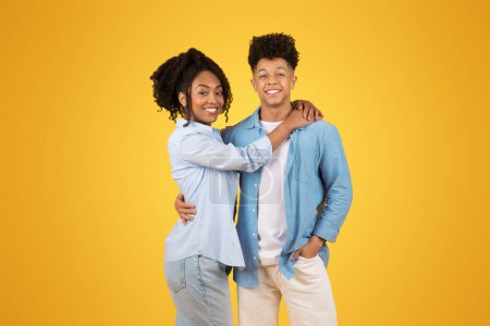 Photo for Two joyful African American young woman and a man, embracing and smiling with a bright yellow background, portraying friendship and cheerful vibes. Ad and offer, relationships, love - Royalty Free Image