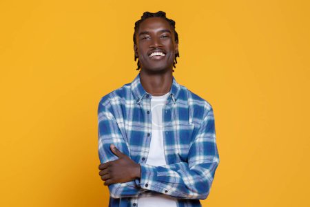 Photo for Handsome Young Black Man Posing With Folded Arms On Yellow Studio Background, Confident Millennial African American Guy Wearing Checkered Shirt Smiling And Looking At Camera, Copy Space - Royalty Free Image