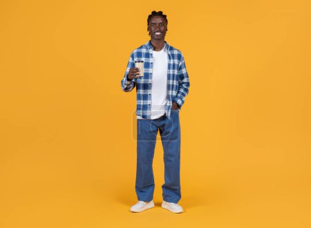 Photo for Handsome young black man holding takeaway coffee in hand and smiling at camera, happy african american male standing confidently against bright yellow background, embodying relaxed lifestyle - Royalty Free Image