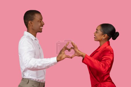 Téléchargez les photos : Heureux couple noir face à face, créant une forme de cœur avec leurs mains, symbolique de l'amour et de la convivialité, sur fond rose romantique - en image libre de droit