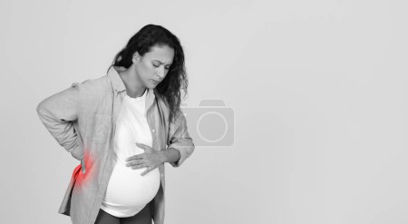 Photo for Unhappy Young Pregnant Woman Having Back Pain Touching Red Ache Zone Standing Over Studio Background. Black And White, Panorama With Empty Space - Royalty Free Image