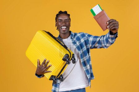 Téléchargez les photos : Concept de voyage. Portrait de heureux jeune homme noir avec valise et passeport dans les mains debout sur fond jaune studio, Africain Américain excité prêt pour les vacances, Copier l'espace - en image libre de droit