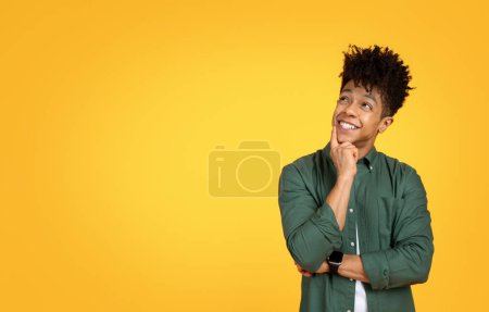 Foto de Emocionado chico negro joven guapo elegante tocando su cara y mirando el espacio de copia para la publicidad, comprobar buena oferta, trato, aislado en el fondo del estudio amarillo - Imagen libre de derechos