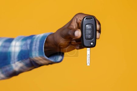 Photo for Closeup of black mans hand presenting set of car keys with remote, unrecognizable african american male suggesting ownership and mobility, standing isolated on yellow studio background, cropped - Royalty Free Image