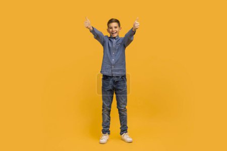 Photo for Cheerful Teen Boy Showing Thumbs Up At Camera With Two Hands, Happy Caucasian Male Child Recommending Something And Having Fun On Yellow Studio Background, Gesturing Sign Of Approval, Full Length - Royalty Free Image