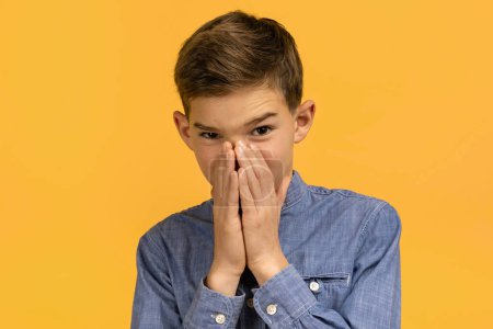 Photo for Teen boy with look of disgust pinching his nose to avoid bad smell, teenage male kid capturing strong reaction to unpleasant odor, his face twisted in grimace, isolated on yellow studio background - Royalty Free Image