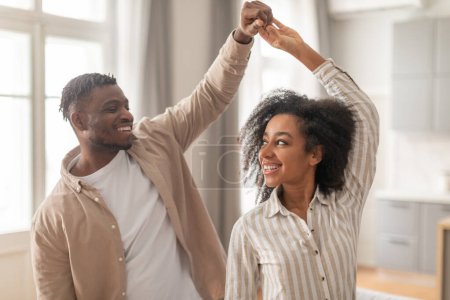 Photo for Party For Two. Happy Loving African American Couple Sharing Their Dance Enjoying Romantic Weekend Moments In Modern Living Room Interior. Shot Of Young Spouses Dancing At Home - Royalty Free Image