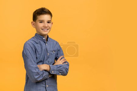 Foto de Retrato de chico adolescente guapo con los brazos doblados de pie sobre el fondo amarillo, niño adolescente feliz mirando a la cámara y sonriendo, posando contra el telón de fondo brillante en el estudio, espacio de copia - Imagen libre de derechos
