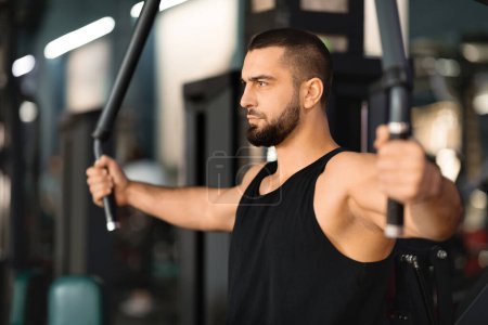 Photo for Concentrated young man in tank top exercising on chest press machine at gym, handsome male athlete working out his pectoral muscles, training in modern sport club interior, closeup shot - Royalty Free Image