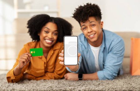 Photo for A smiling african american young couple on the floor shows off a smartphone and a credit card, suggesting a convenient online transaction or enjoyable shopping experience at home - Royalty Free Image