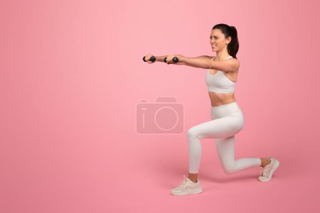 Photo for Happy strong millennial caucasian woman in white sportswear, squats with dumbbells, enjoy training, active lifestyle, isolated on pink background. Health care, sport and weight loss - Royalty Free Image