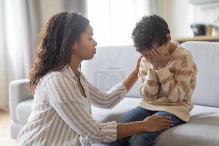 Foto de Cuidar a una mujer afroamericana consolando a su hijo molesto en casa, primer plano de una madre negra cariñosa apoyando a un niño masculino en casa, amando a mamá calmando a un niño llorando sentado en el sofá en la sala de estar - Imagen libre de derechos