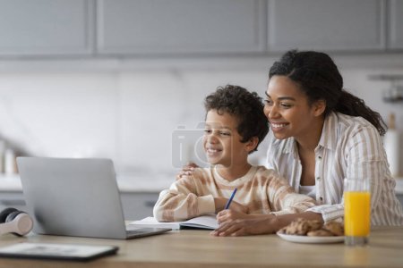 Photo for Remote Education. Black Mom And Little Son Using Laptop At Home Together, Happy Preteen Boy And His Beautiful Mother Looking At Computer Screen And Smiling, Enjoying Distance Learning Programs - Royalty Free Image