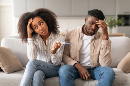 Photo for Unwanted Pregnancy. Upset Child Free African American Couple Holding Positive Pregnancy Test, Feeling Stressed Sitting On Couch At Home. Unplanned Childbirth, Unintended Pregnancies Concept - Royalty Free Image