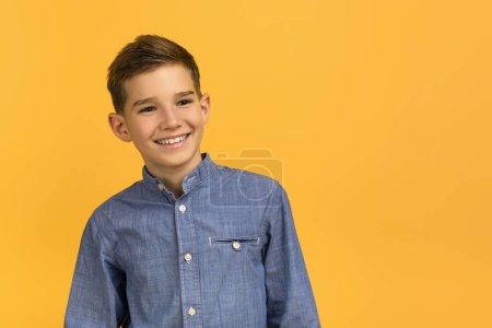 Téléchargez les photos : Joyeux adolescent en jean casual posant en toute confiance sur fond de studio jaune vif, adolescent gai garçon regardant ailleurs et souriant, représentant l'optimisme des jeunes, l'espace de copie - en image libre de droit