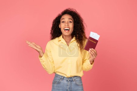 Foto de Mujer negra emocionada, radiante de felicidad, sosteniendo su pasaporte y boletos de avión mientras está de pie sobre un animado fondo rosa, perfecto para transmitir emoción y anticipación de viaje - Imagen libre de derechos