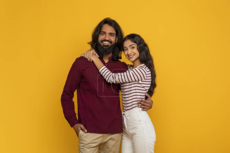 Photo for Happy young indian man and woman embracing on yellow studio background, smiling at camera. Millennial hindu couple hugging, posing together, copy space. Relationships, marriage, love - Royalty Free Image