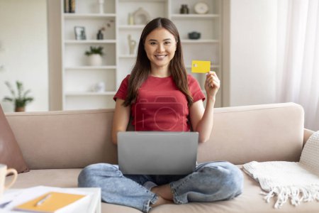 Photo for Online Banking Concept. Portrait Of Happy Young Asian Woman With Laptop And Credit Card Sitting On Couch In Living Room, Smiling Korean Woman Enjoying Making Payments From Home, Free Space - Royalty Free Image