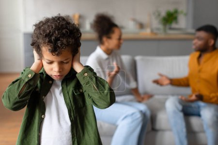 Photo for Preteen boy with curly hair covers his ears, feeling distressed as his parents have discussion in the background, depicting family conflict, focus on child - Royalty Free Image