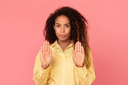 Photo for Serious black woman in yellow blouse making stop sign with her hands, with concerned expression, standing against plain pink background - Royalty Free Image