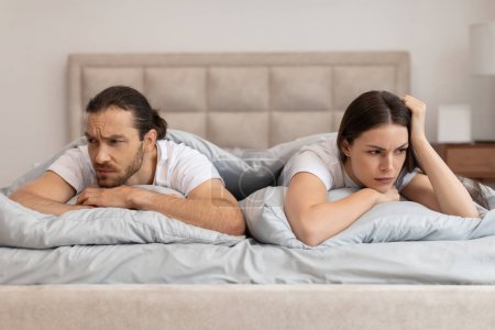 Téléchargez les photos : Homme et femme couchés au lit avec des visages anxieux, détournés les uns des autres, suggérant tension et préoccupation dans leur relation - en image libre de droit