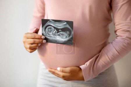 Téléchargez les photos : Femme enceinte noire méconnaissable montrant sa photo d'échographie de bébé, jeune femme enceinte montrant la première photo de son enfant, jouissant d'un temps de maternité heureux, image recadrée, gros plan - en image libre de droit