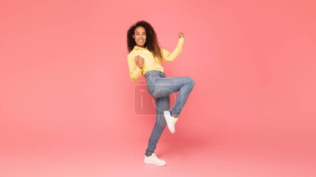 Enthusiastische schwarze Frau in Aufregung ballt ihre Fäuste und Gesten ja vor leuchtendem rosa Hintergrund, ideal, um Positivität, Erfolg und Enthusiasmus zu demonstrieren, volle Länge