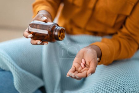 Foto de Primer plano de las manos de las mujeres afroamericanas mientras vierte pastillas rosadas de una botella de medicina marrón, posiblemente indicando manejo de salud, rutina de medicamentos o suplementación de vitaminas. - Imagen libre de derechos