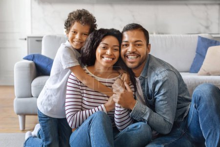Photo for Happy Loving Family. Portrait of cheerful African American parents and son sitting on floor at home, posing for photo, smiling boy embracing parents, enjoying time together, free space - Royalty Free Image
