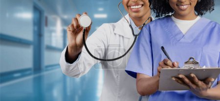 Photo for A smiling women doctor holding a stethoscope towards the camera with a nurse using a clipboard in the background, representing a friendly and professional healthcare service - Royalty Free Image