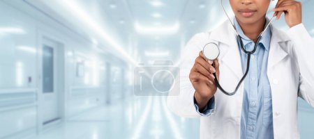 Téléchargez les photos : Une femme médecin confiante dans un manteau blanc tenant un stéthoscope dans un couloir d'hôpital lumineux, symbolisant le professionnalisme des soins de santé et l'état de préparation médicale en clinique, panorama - en image libre de droit