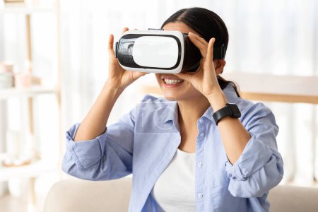 Téléchargez les photos : Modern rester à la maison passe temps. Femme asiatique en réalité virtuelle casque explorant le cyberespace à l'intérieur. Jeune femme chinoise en lunettes VR jouer à un jeu d'ordinateur interactif, espace de copie - en image libre de droit