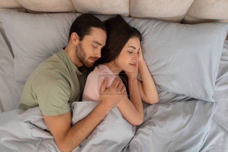 Téléchargez les photos : Contenu jeune couple dans une étreinte chaleureuse, couché près du lit, avec des expressions de paix et d'intimité, suggérant confort et affection - en image libre de droit