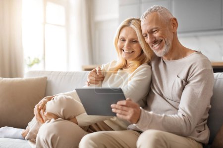 Photo for Happy Senior Couple Enjoying Digital Gadget World Using Their Tablet Computer, Websurfing And Watching Film Online In Modern Living Room At Home, Copy Space. Retirement And Internet Fun Concept - Royalty Free Image