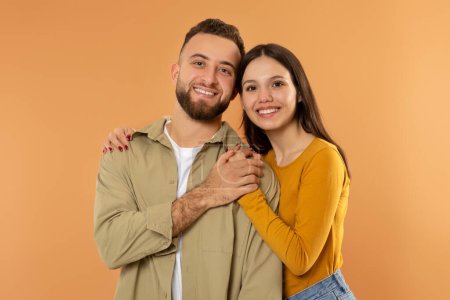 Photo for Real Love. Happy Young Family Couple Hugging And Holding Hands Symbolizing Their Romantic Bond, Smiling To Camera While Posing Over Orange Studio Background, Portrait Shot - Royalty Free Image