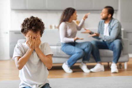 Photo for Upset black preteen boy covering his face with hands while his parents arguing at home, depicting domestic family conflict, depressed african american male kid feeling lonely and abandoned - Royalty Free Image