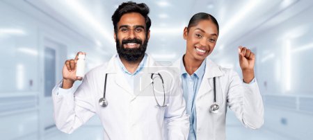 Photo for Hindu, african american medical professional smiling confidently, raising their hands in a victory gesture, one holding a pill bottle, in a hospital corridor, recommends health care and treatment - Royalty Free Image
