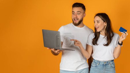 Photo for A glad european man and a woman holding a laptop and a credit card look amazed, possibly at an online shopping deal, while standing against a vibrant orange background, panorama - Royalty Free Image