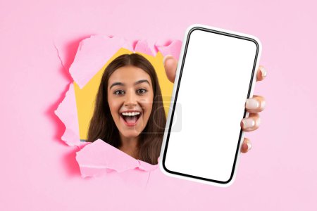 Photo for Mobile Offer. Excited european millennial lady showing big modern smartphone with blank mockup screen through ripped pink paper backdrop, presenting device or new application. Collage - Royalty Free Image