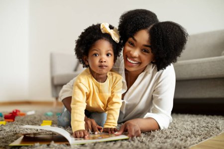 Photo for Happy african american young mother and little daughter playing at home, laying on floor, reading books, mom entertaining her toddler kid with various toys. Child development - Royalty Free Image