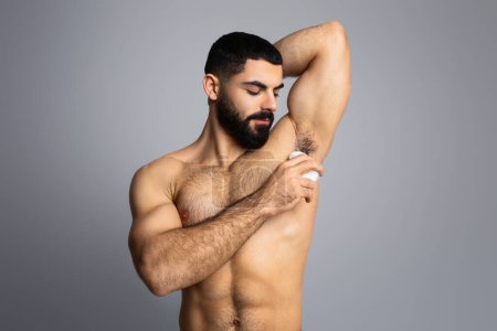 Photo for Male Hygiene Routine. Man care concept. Muscular handsome middle eastern shirtless young man using antiperspirant deodorant isolated on grey studio background - Royalty Free Image