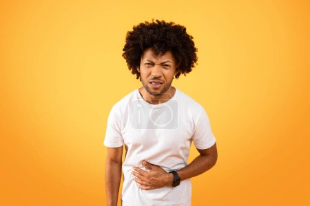 Photo for Unhealthy millennial black man suffering with stomach pain, feeling sick, unwell. Unhappy african american guy touching his belly, isolated on colorful studio background - Royalty Free Image