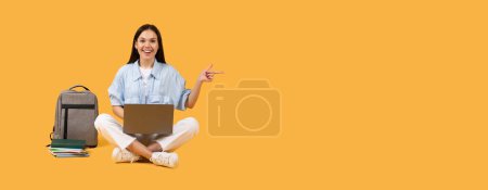 Photo for Enthusiastic european female student sitting cross-legged with laptop on lap, pointing to the side at free space, with books and backpack on yellow background, panorama - Royalty Free Image