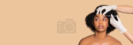 Foto de Mujer afroamericana serena recibiendo inyección facial cosmética, con expresión tranquila, mirando a un lado el espacio libre sobre fondo beige, panorama - Imagen libre de derechos